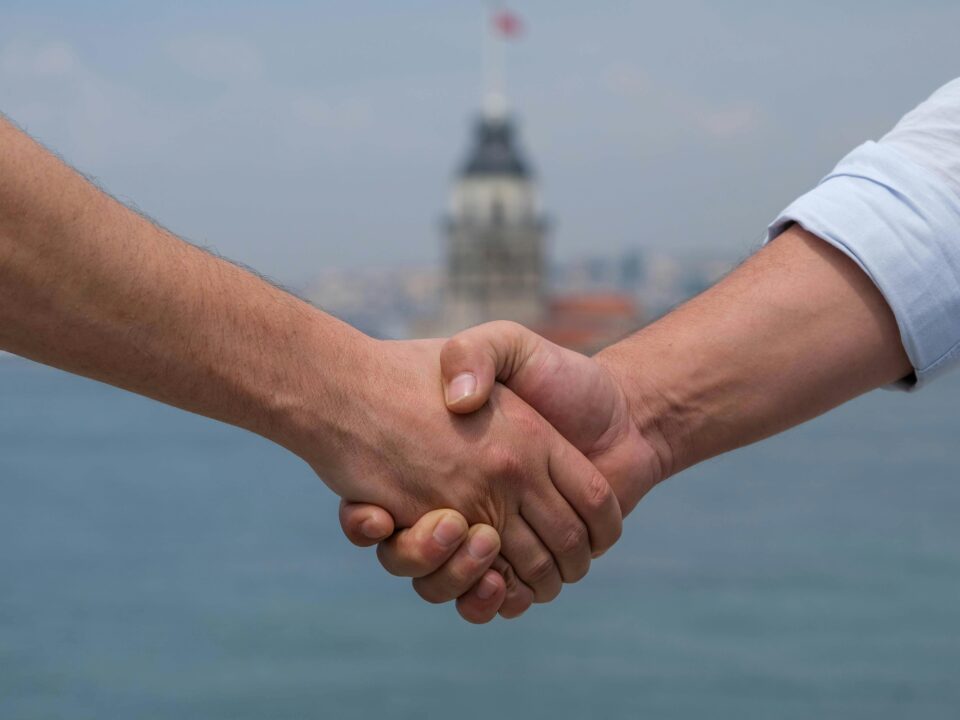 Close-up of handshake at Bosphorus with Maiden's Tower in background, symbolizing cooperation.